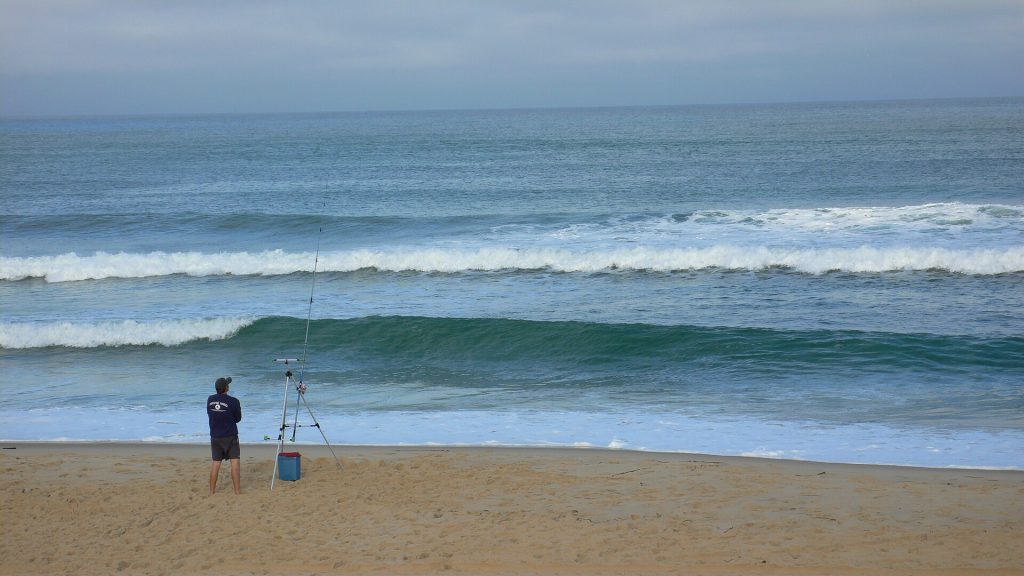 Un pêcheur en surfcasting sur une plage de l’Atlantique, face aux vagues.